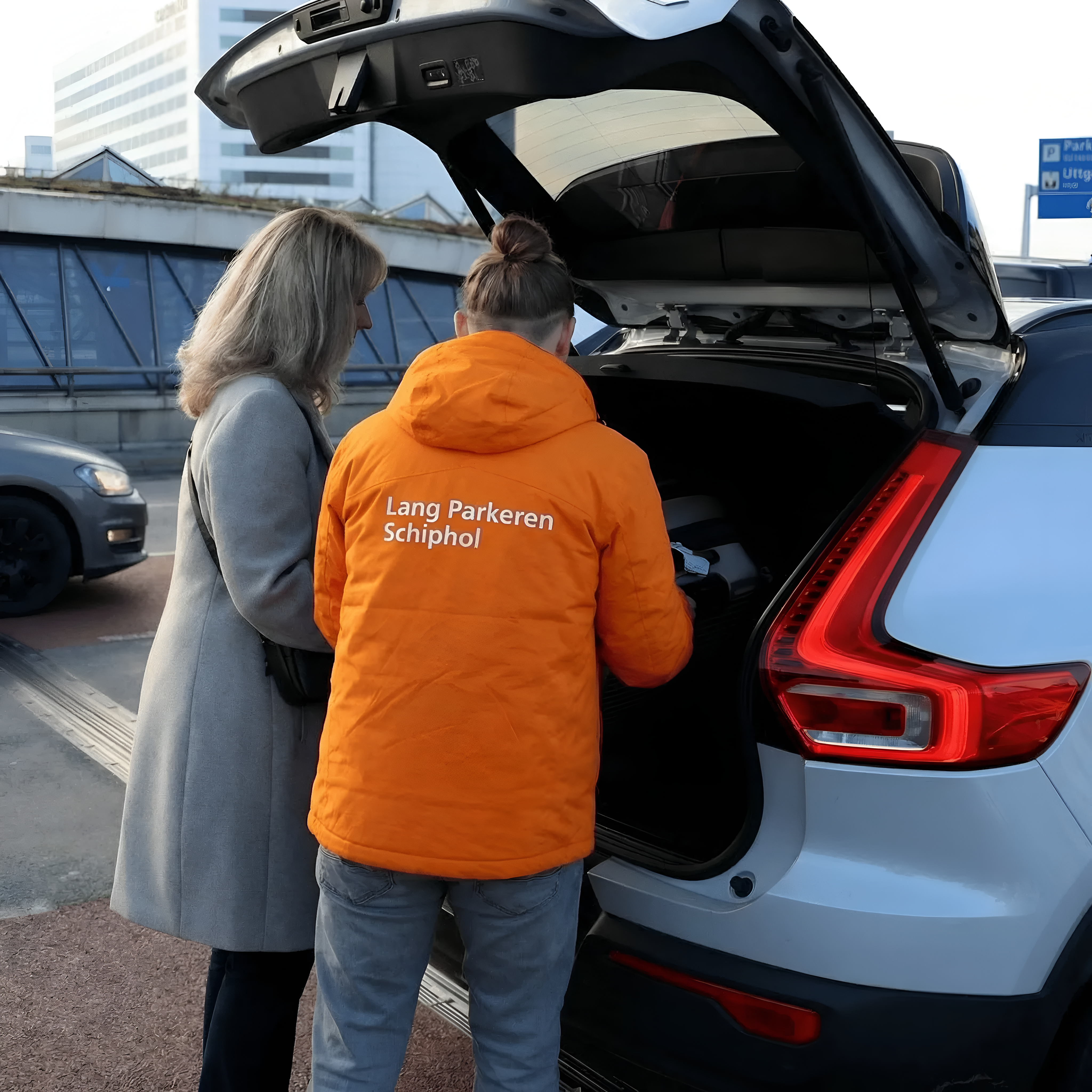 Medewerker van Lang Parkeren Schiphol tilt een koffer uit de kofferbak terwijl de reiziger toekijkt bij de vertrekhal.