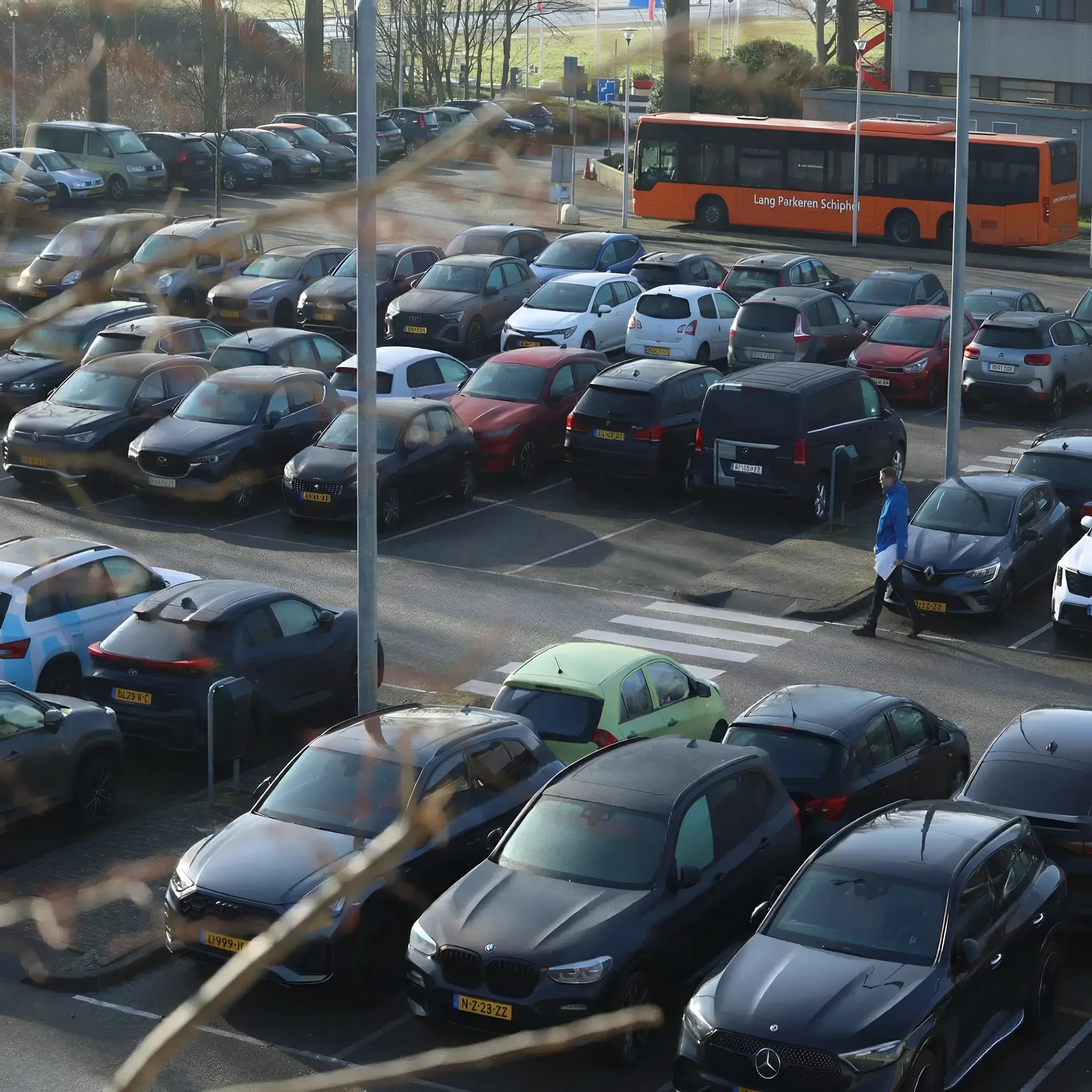 Parkeerterrein van Lang Parkeren Schiphol met rijen geparkeerde auto’s met Nederlandse gele kentekenplaten en de oranje shuttlebus.