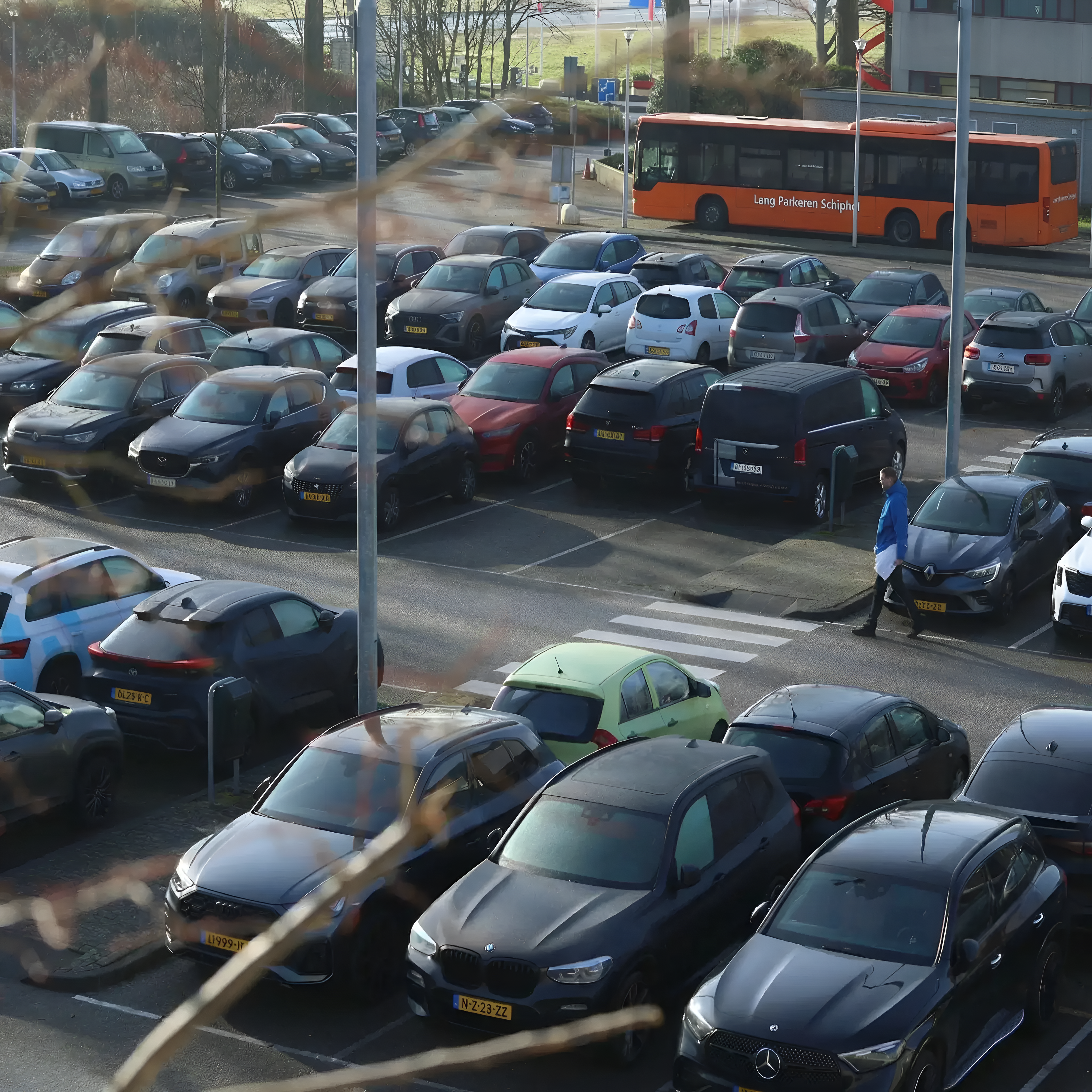 Parkeerterrein van Lang Parkeren Schiphol met rijen geparkeerde auto’s met Nederlandse gele kentekenplaten en de oranje shuttlebus.